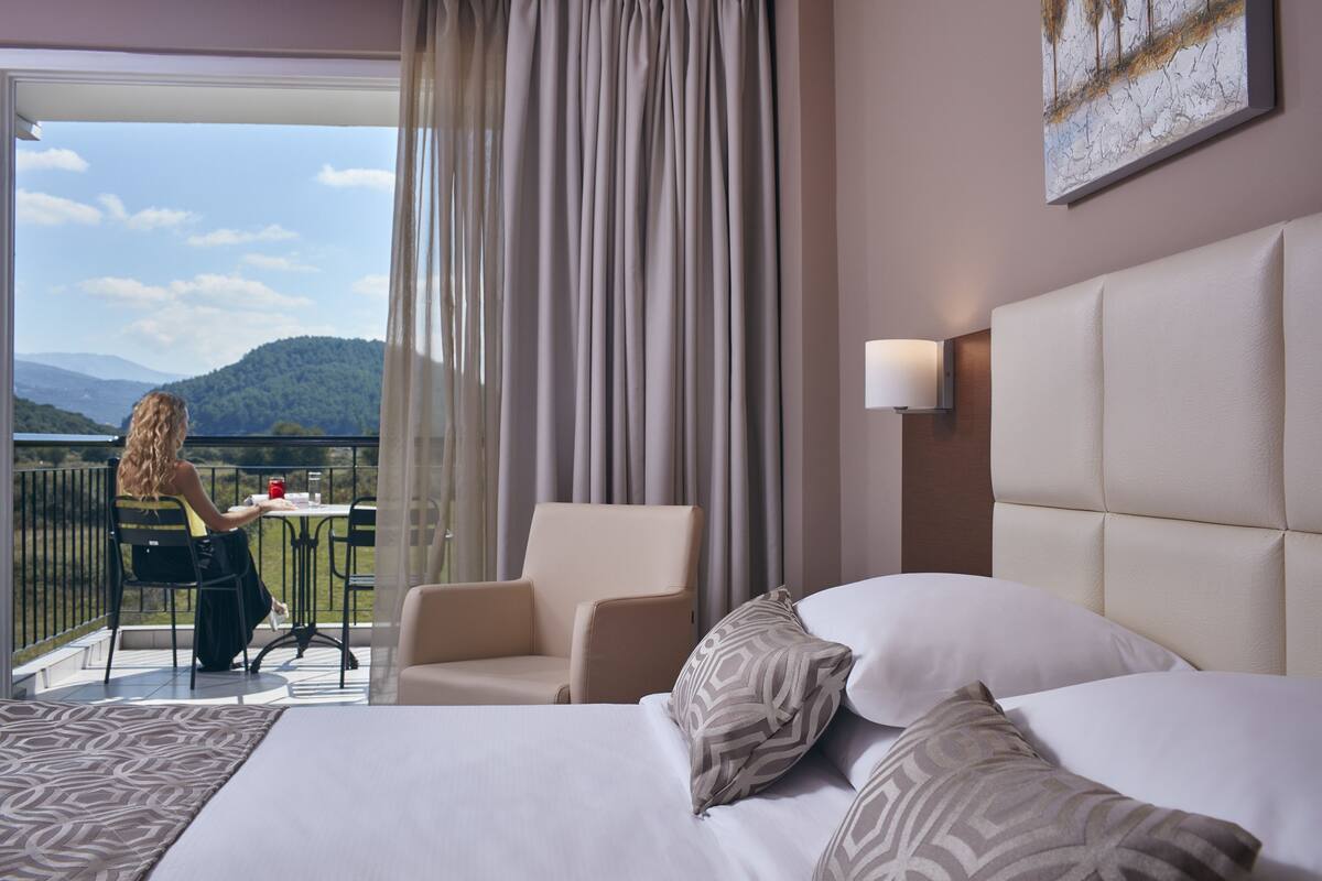 A hotel room with a bed, a chair, a table, and a view of the outdoors.
