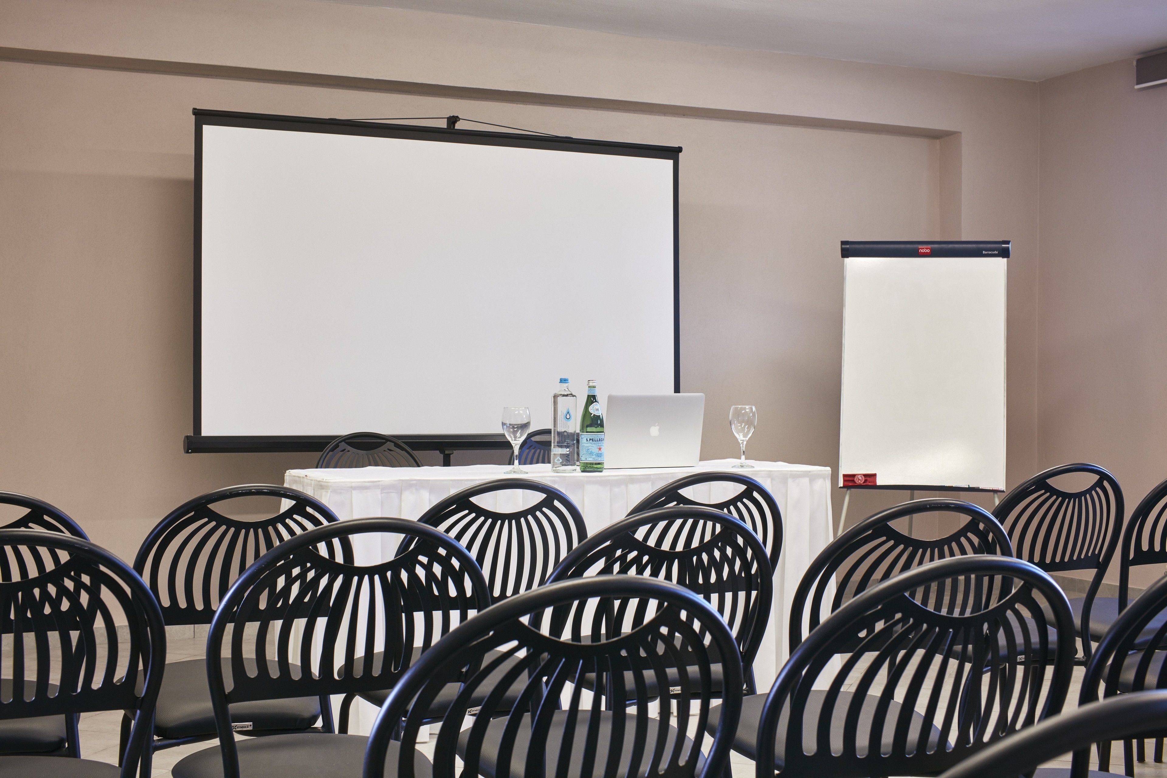 A conference room with a large projection screen, a whiteboard, and several chairs arranged around a table with a laptop, water bottles, and glasses.
