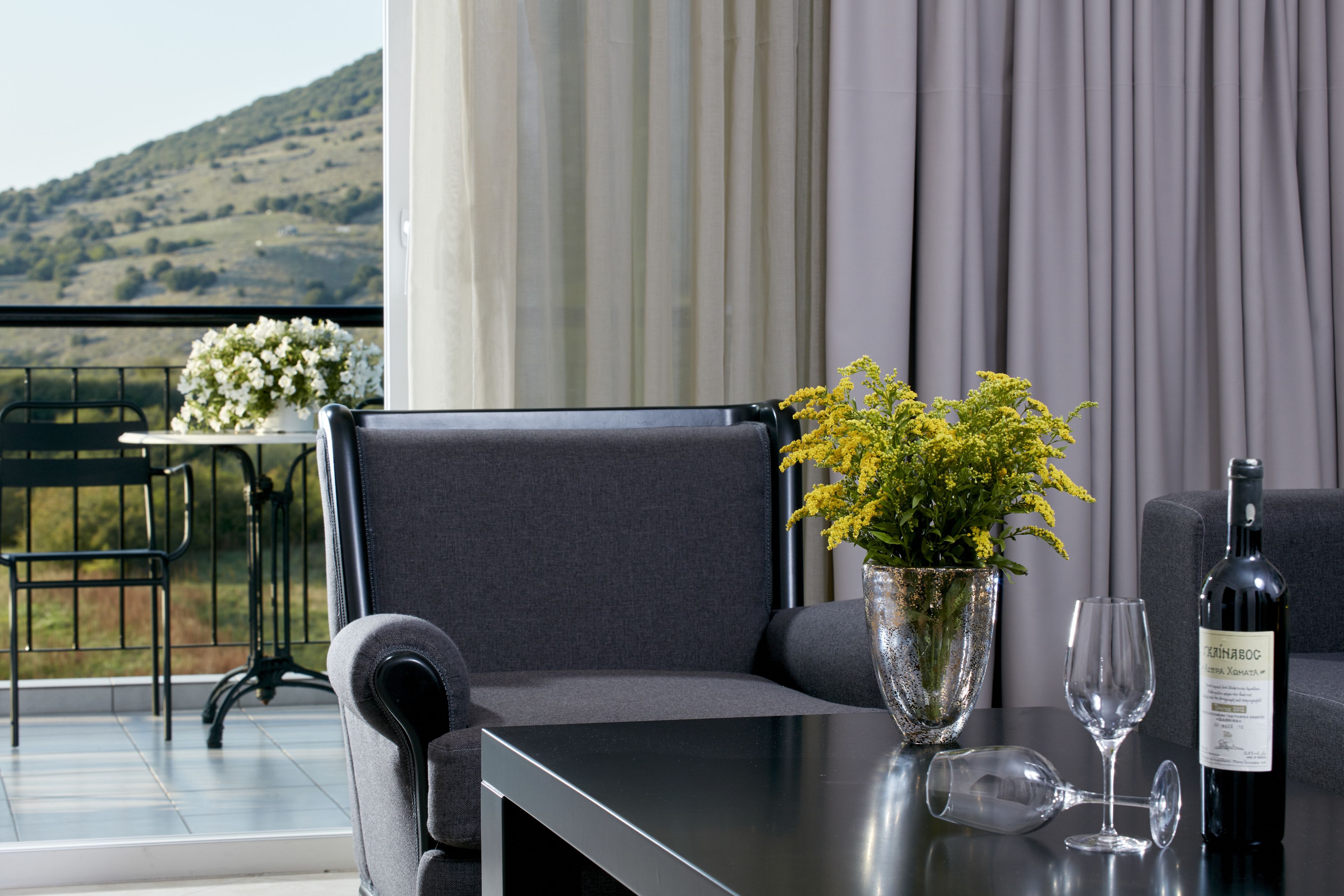 Ein Balkon mit Tisch, Stuhl, Blumen in einer Vase, einer Weinflasche und einem Weinglas.