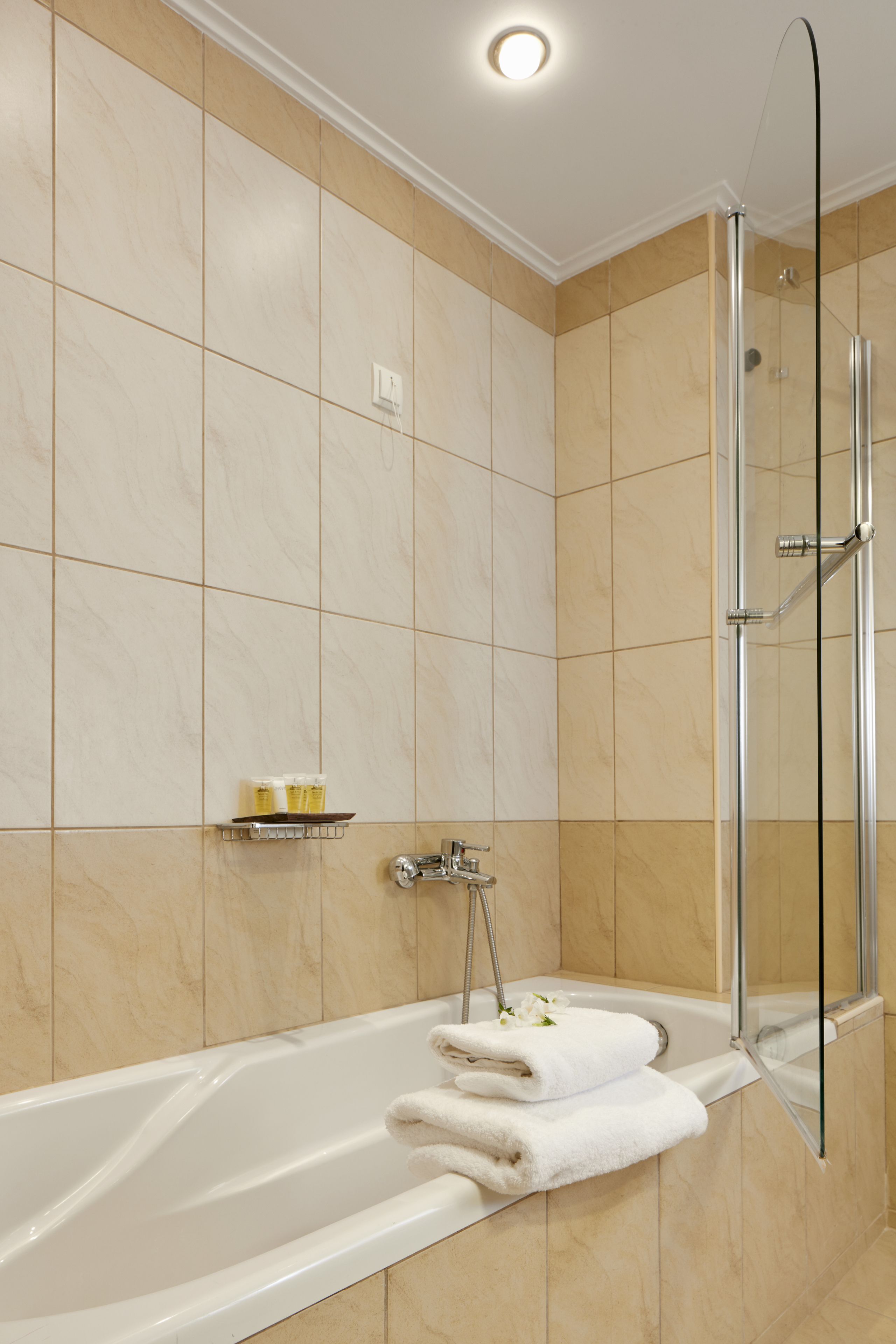 A modern bathroom with a glass-enclosed shower, a white bathtub, and a shelf with toiletries.