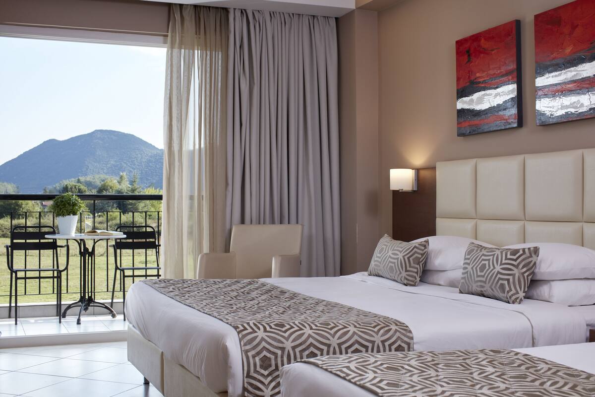 A hotel room with two beds, a balcony with a table and chairs, and a mountain view.