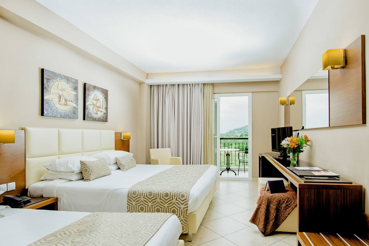 A hotel room with two beds, a desk, a chair, a TV, and a balcony with a view.