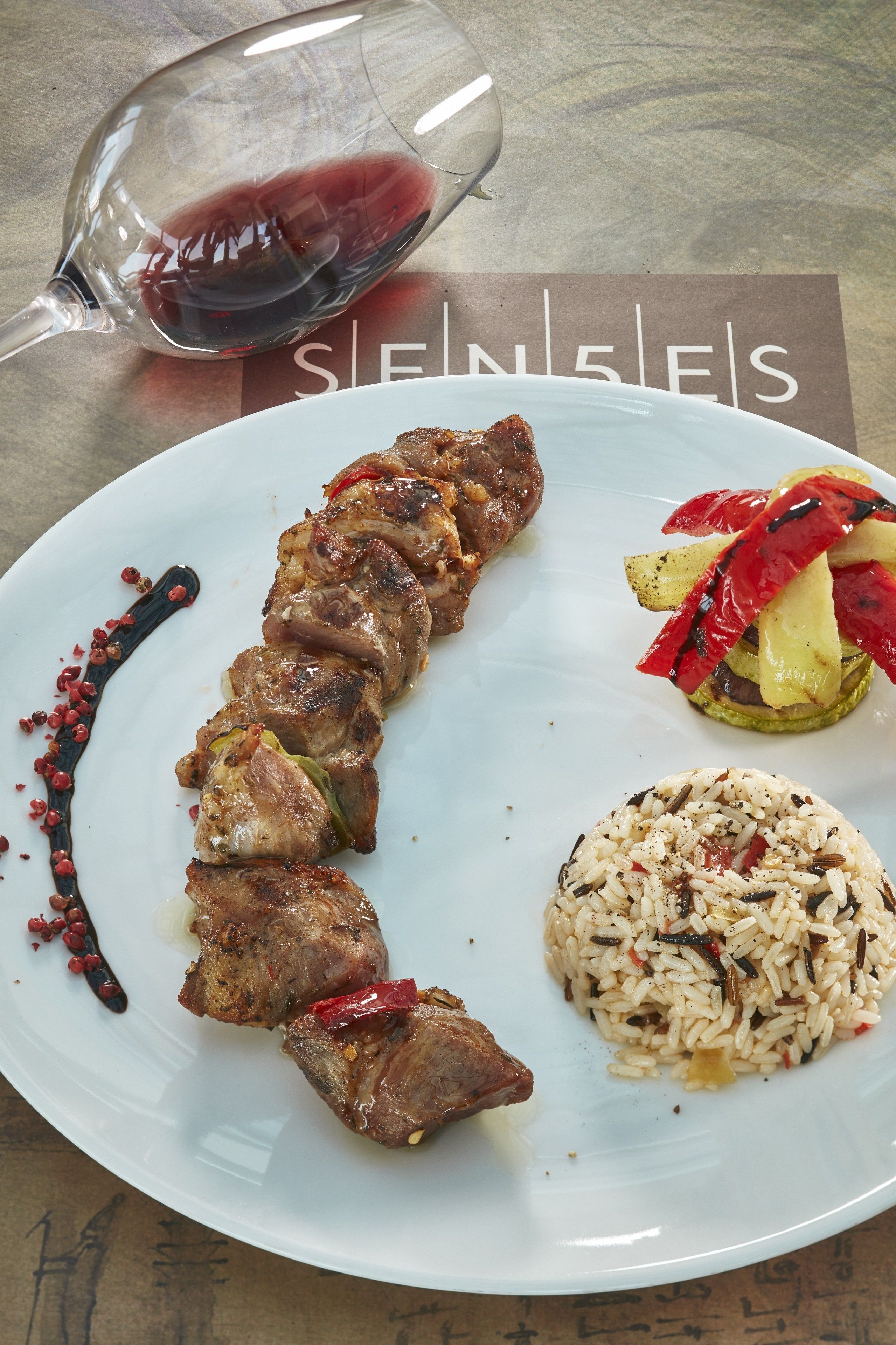 A plate with grilled meat, grilled vegetables, and rice, accompanied by a glass of red wine.