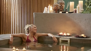 Une femme se détend dans un bain à remous, avec des bougies et une statue de Bouddha en arrière-plan.