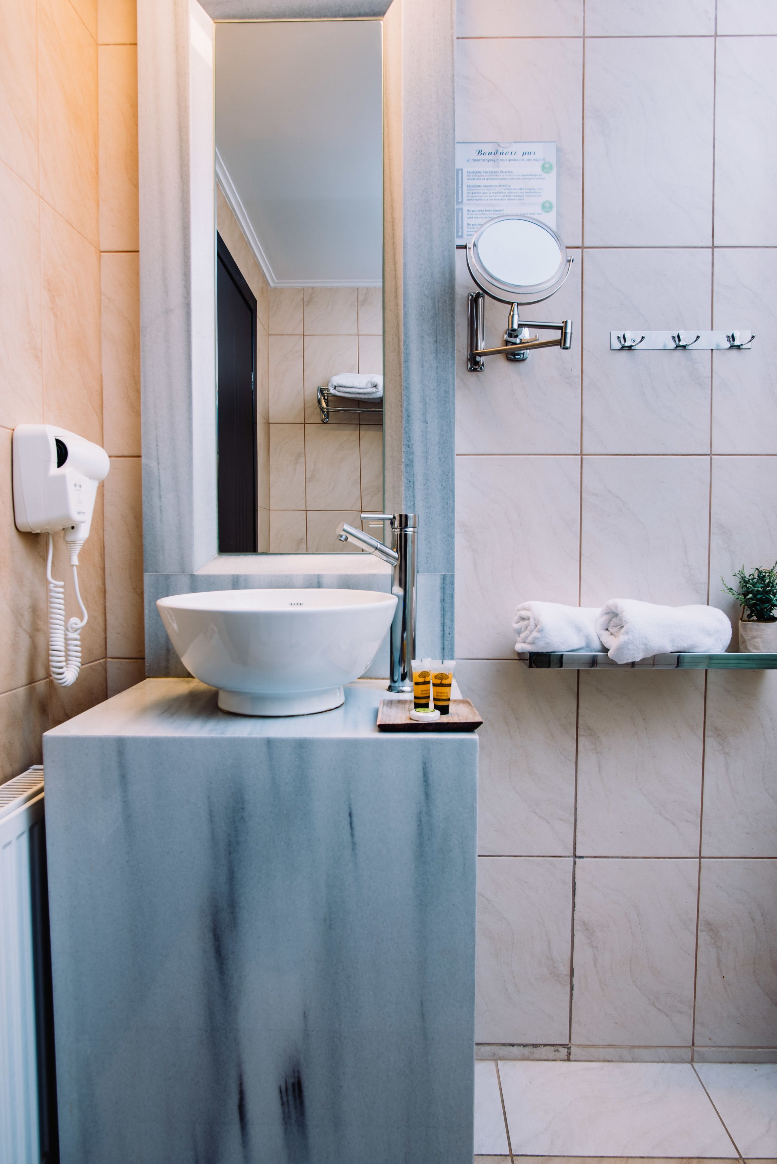 Een badkamer met een wit wastafel, een spiegel, een handdoekhouder en een handdroger.