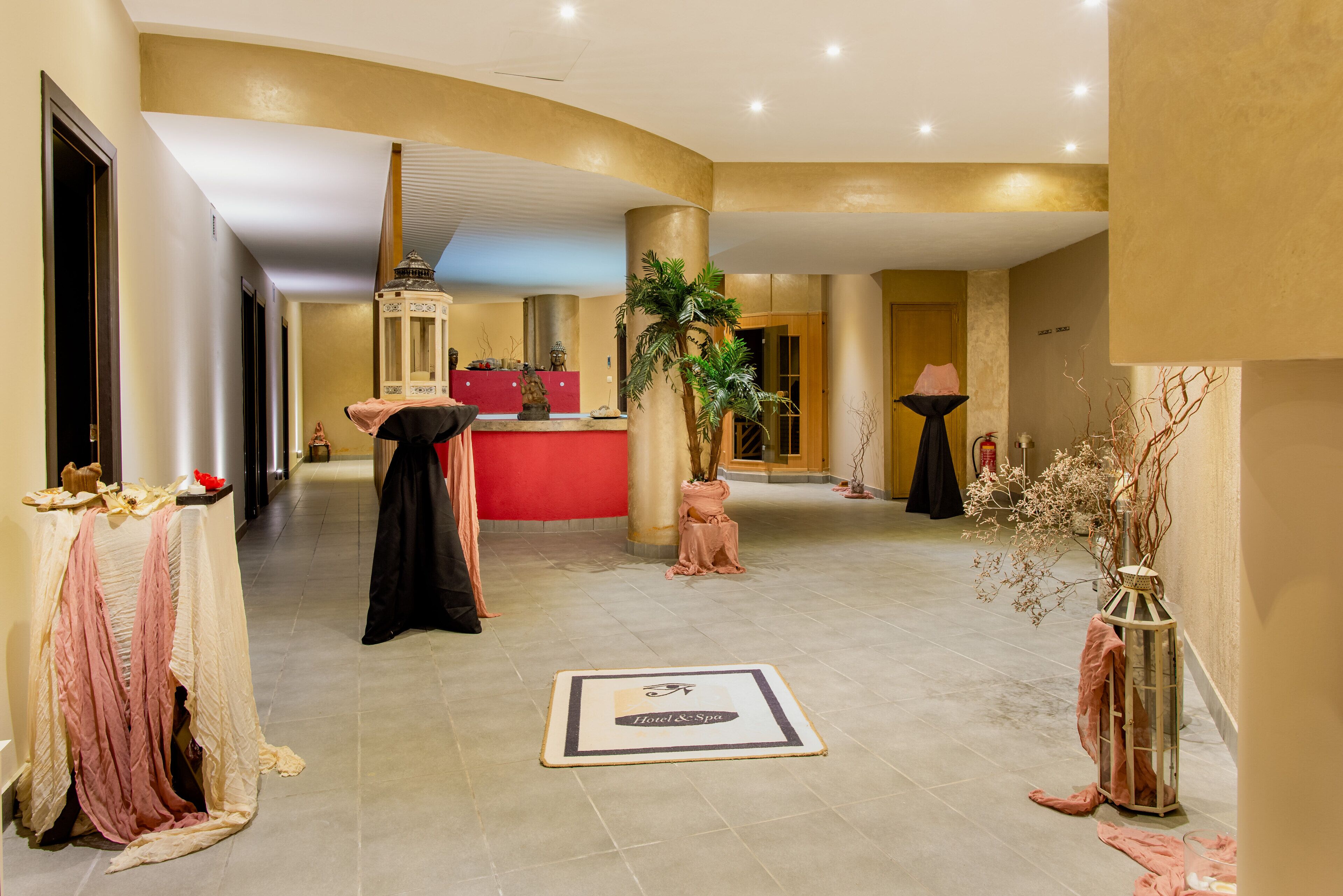 Un hall d’hôtel avec un comptoir d’accueil, un comptoir rouge, une grande plante et une lanterne décorative.