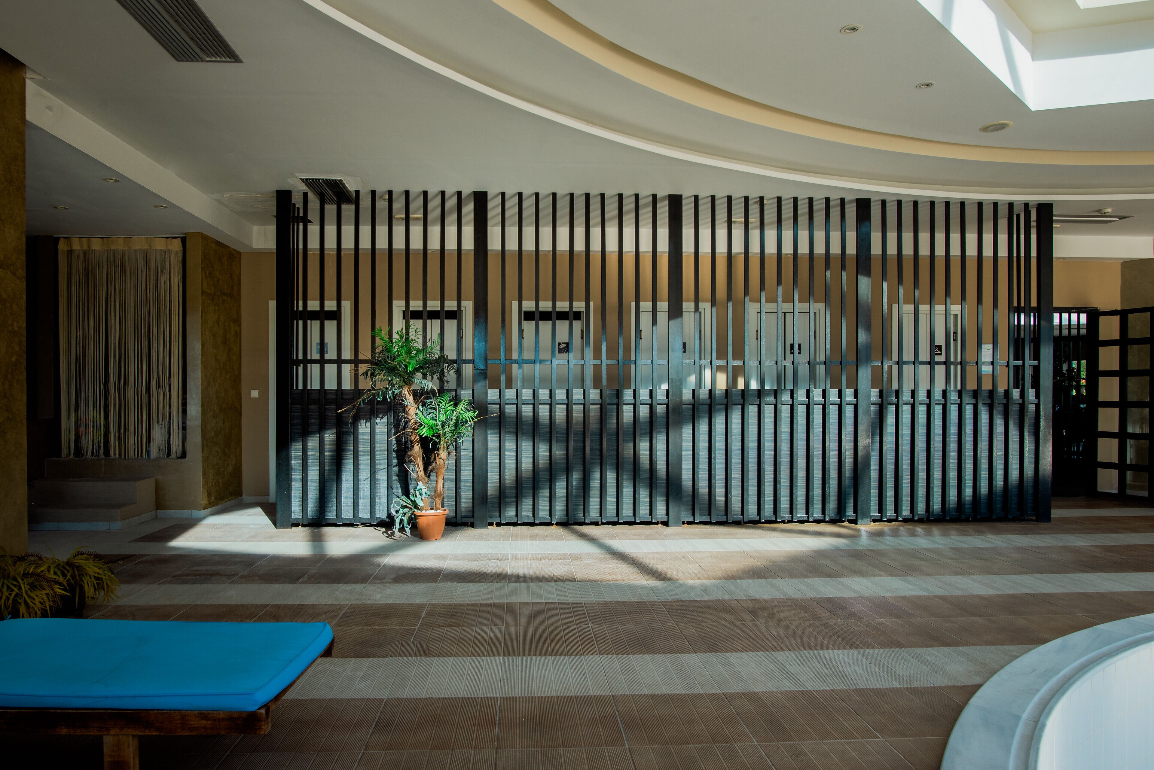 Un área de piscina interior moderna con techo curvo, una silla de descanso azul y una planta en maceta.