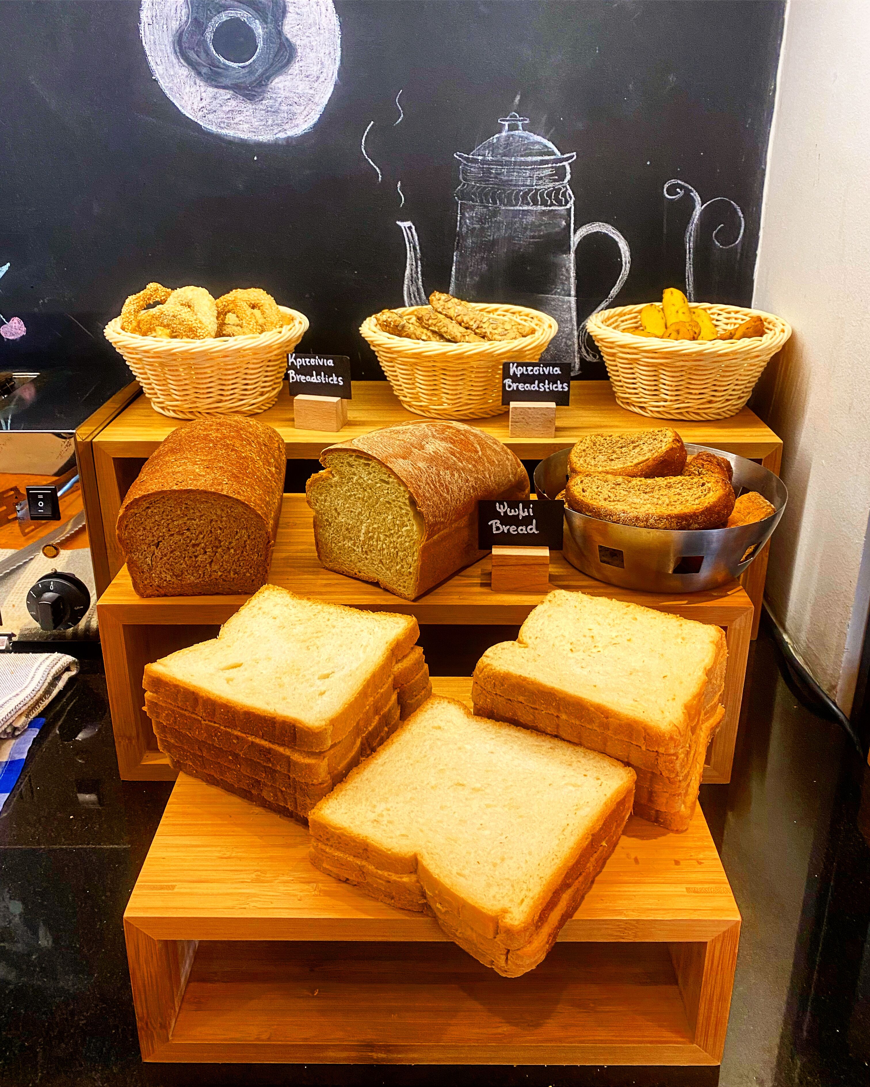 A display of various breads and pastries on wooden shelves with labels.