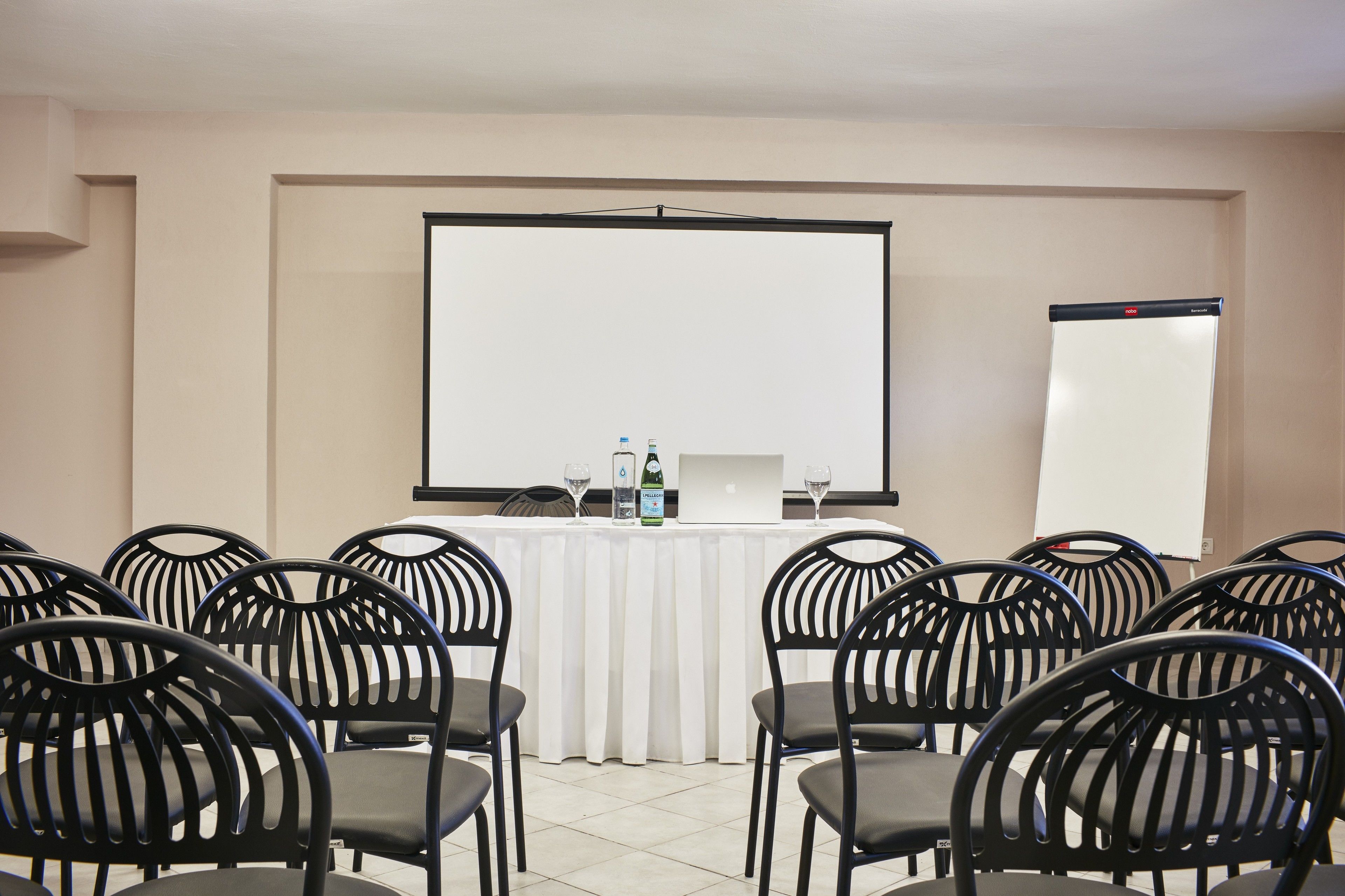 A conference room with a white table, black chairs, a projector screen, and a whiteboard.