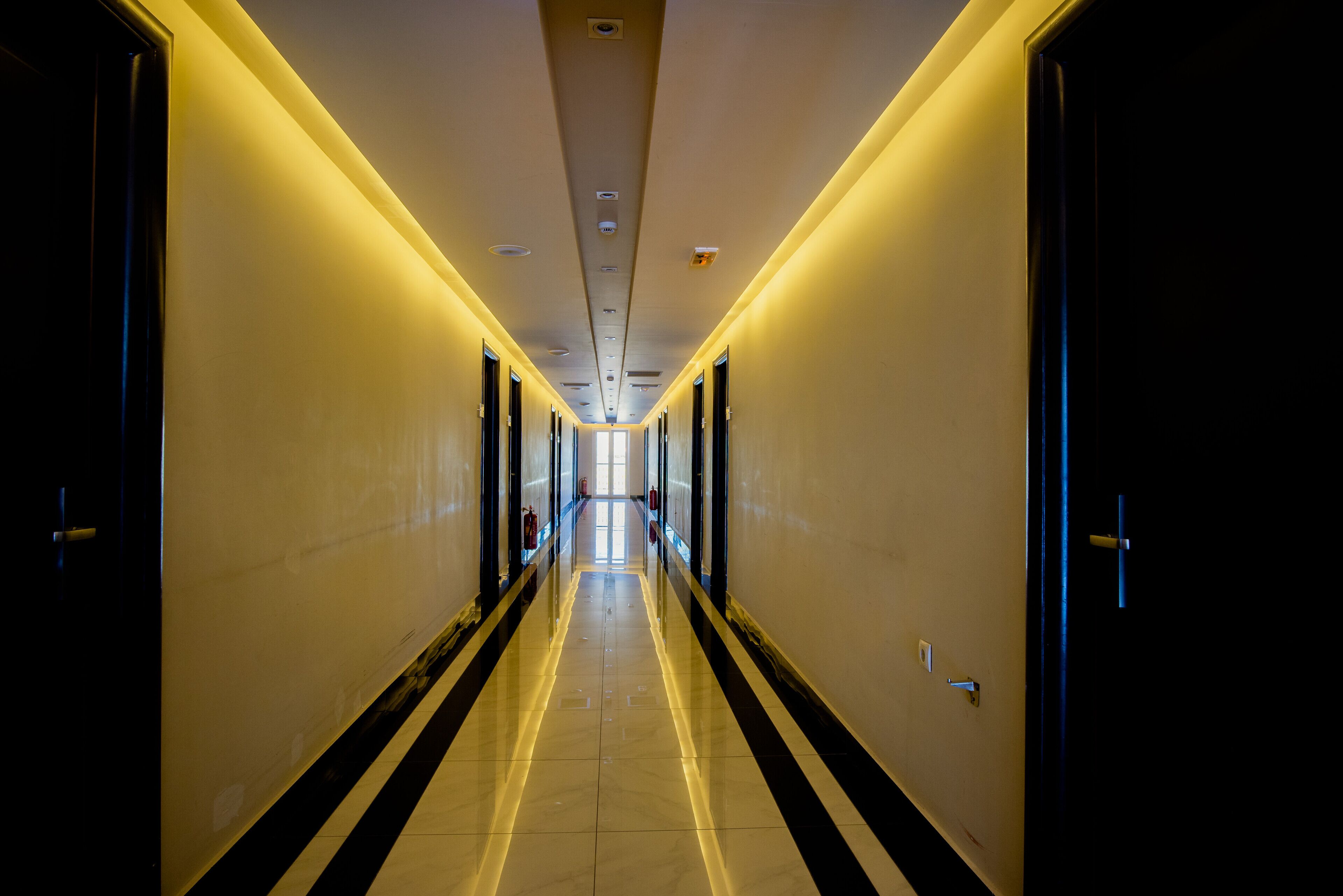 Un pasillo largo y estrecho con puertas a ambos lados, que conduce a un extremo luminoso.