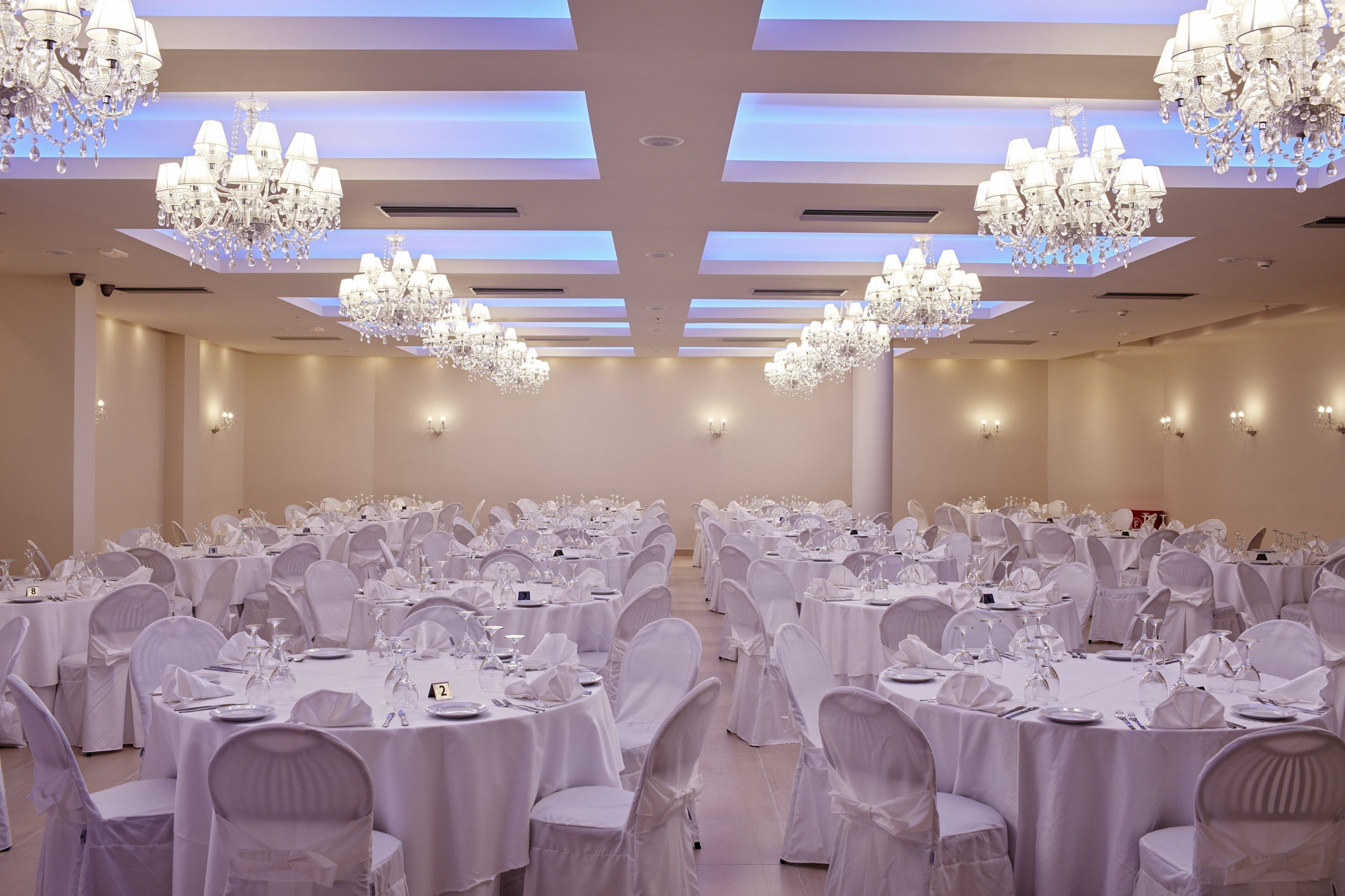 Un salón de banquetes con mesas redondas, manteles blancos y candelabros.