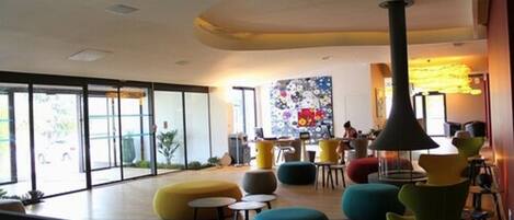 A modern interior with large windows, colorful seating, and a central art piece.