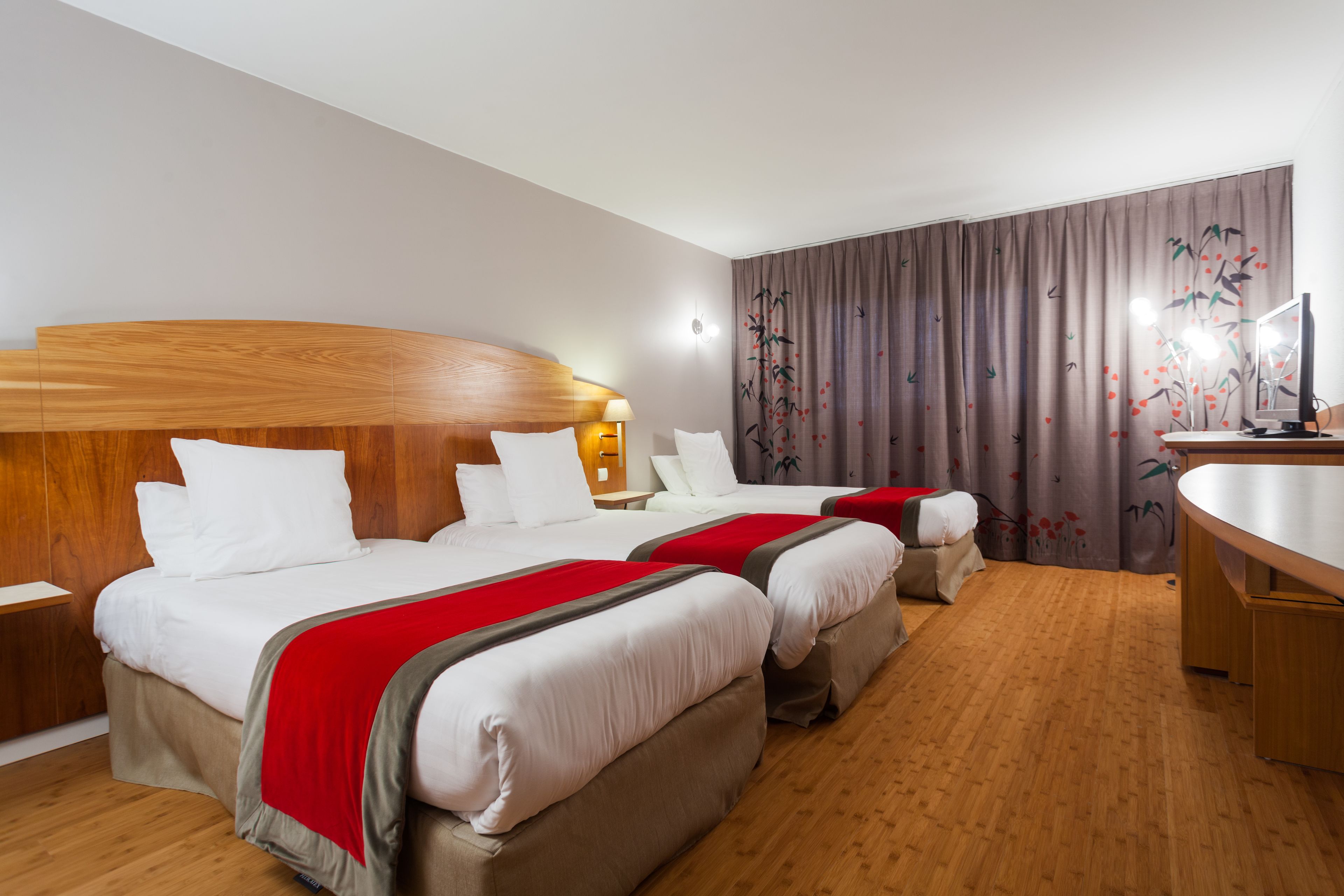 Ein Hotelzimmer mit zwei Betten, einem Holzkopfstück, Nachttischen, einem Schreibtisch und einem großen Fenster mit Vorhängen.
