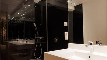 A modern bathroom with a large mirror, a white sink, and a glass-enclosed shower.