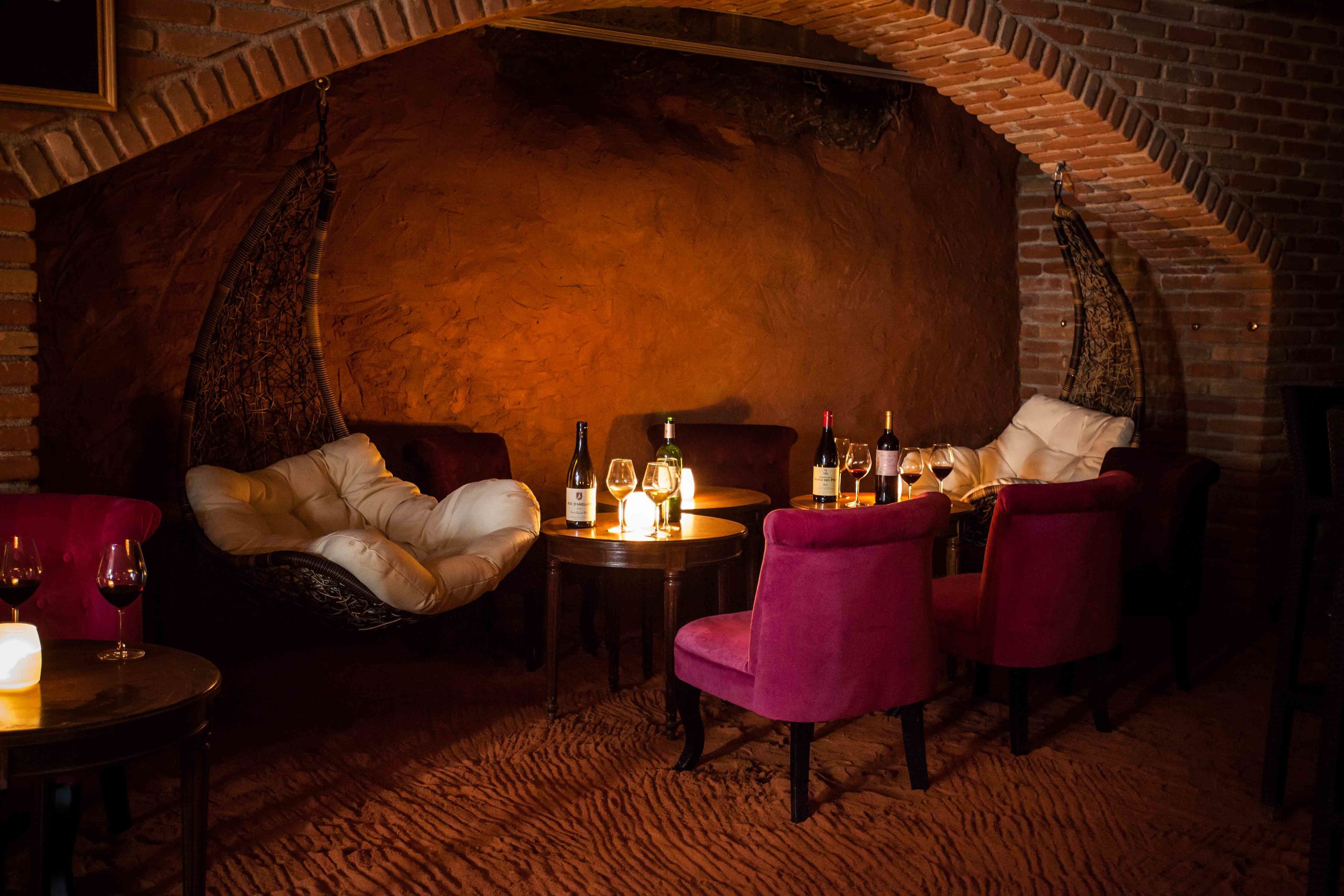 A cozy room with a brick wall, a hanging chair, and a table with wine glasses and bottles.