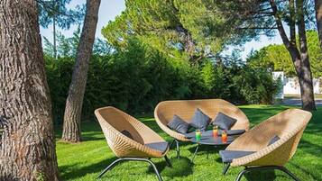 An outdoor seating area with wicker chairs and a table, surrounded by trees and grass.