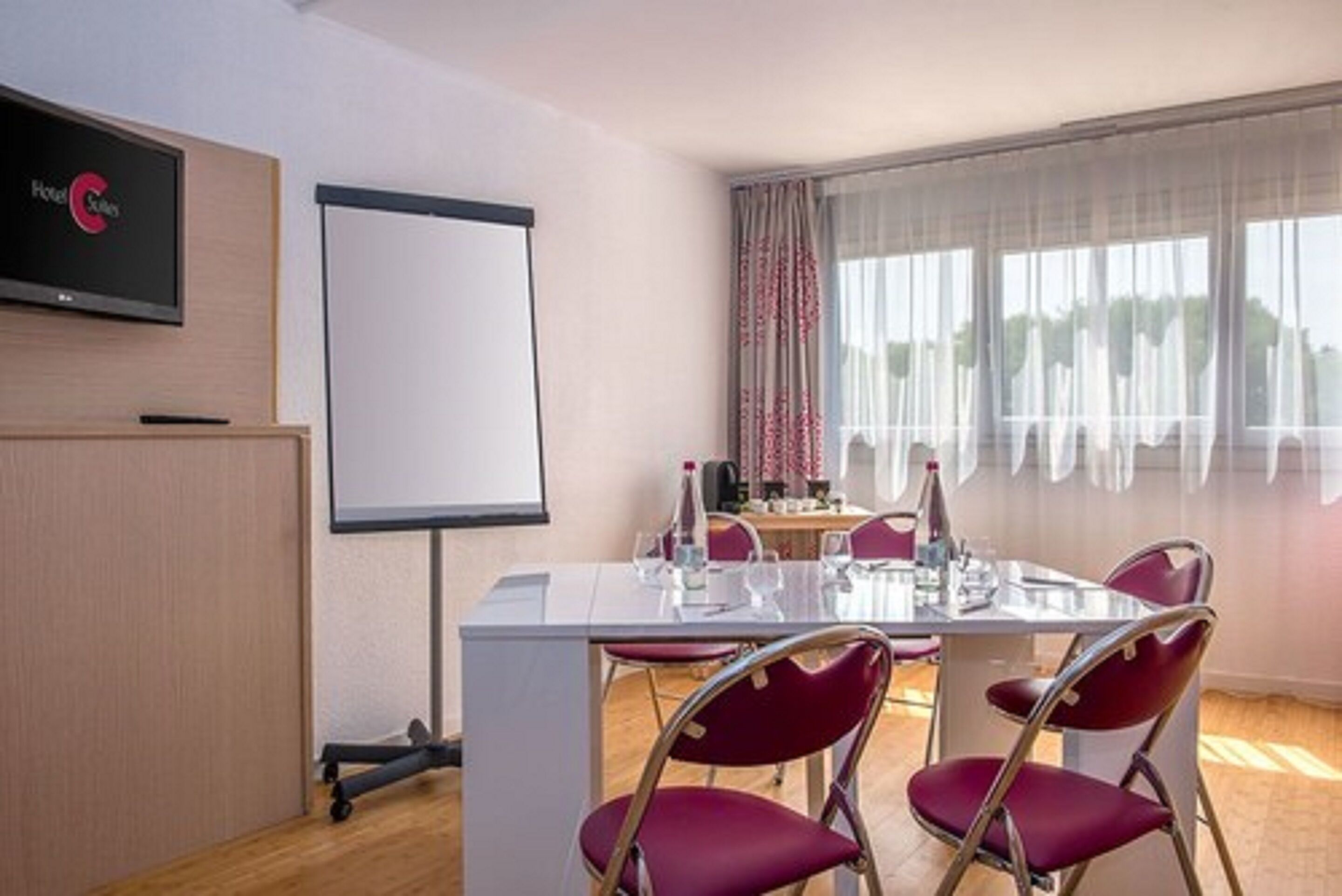 A conference room with a whiteboard, a TV screen, and a table set for four with red chairs.