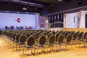Un salón de conferencias con filas de sillas mirando hacia un escenario con un letrero que dice 'Hotel Suites'.