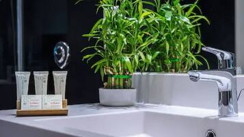 A bathroom with a white sink, a mirror, and a potted plant. There are three tubes of cream on the counter.
