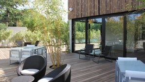 An outdoor patio with wicker furniture, glass tables, and a bamboo plant. - C Suites (Nîmes)