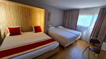 Ein Hotelzimmer mit zwei Betten, einem hölzernen Kopfteil, einem Sessel und einem Fenster mit Vorhängen.