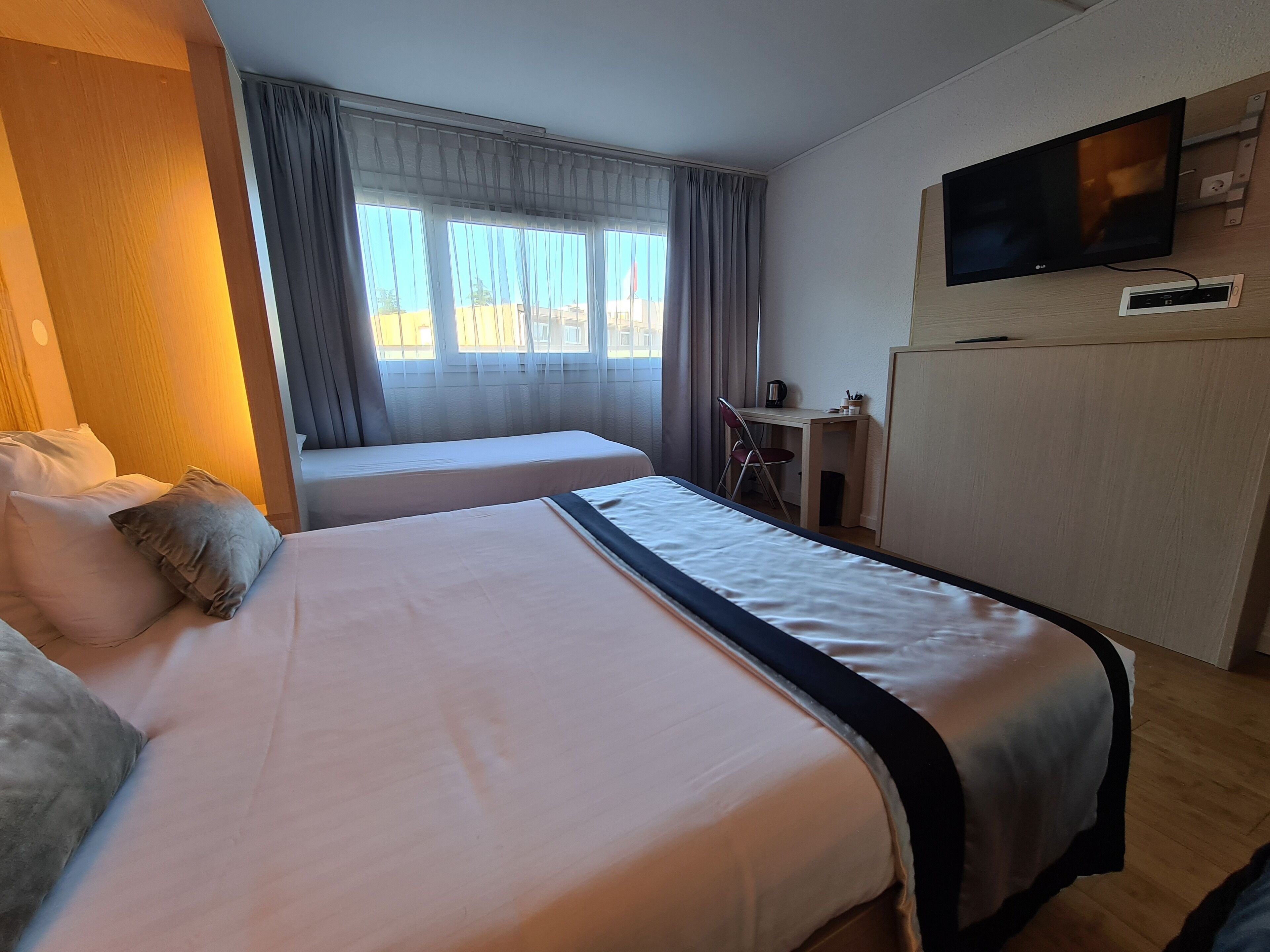 A hotel room with two beds, a desk, a chair, a television, and a window with curtains.