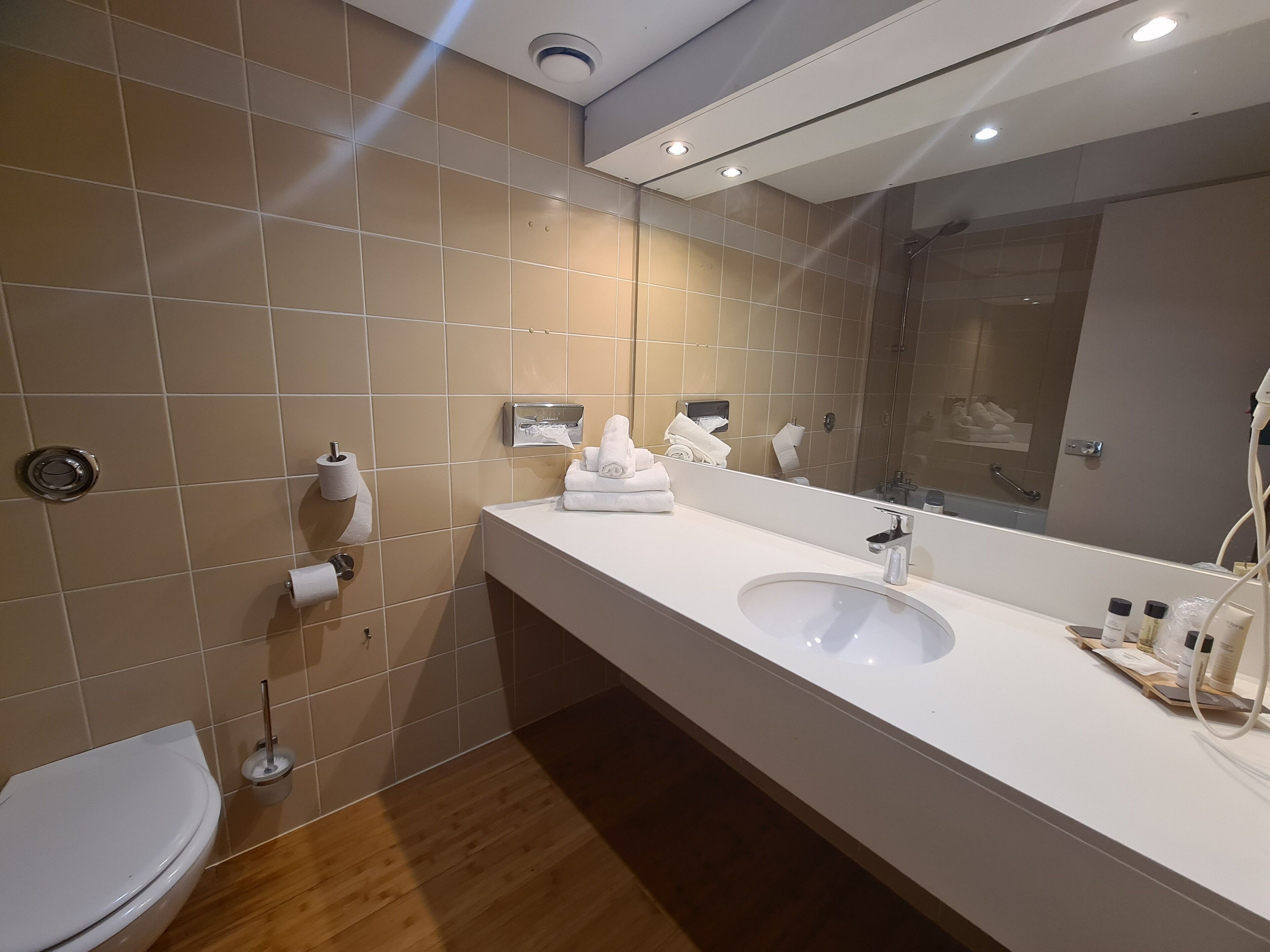 Une salle de bain moderne avec un lavabo blanc, un miroir et des carreaux de couleur beige.