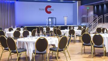 Une salle de conférence équipée de tables et de chaises rondes, d’un pupitre et d’un grand écran affichant le logo « Hotel Suites ».