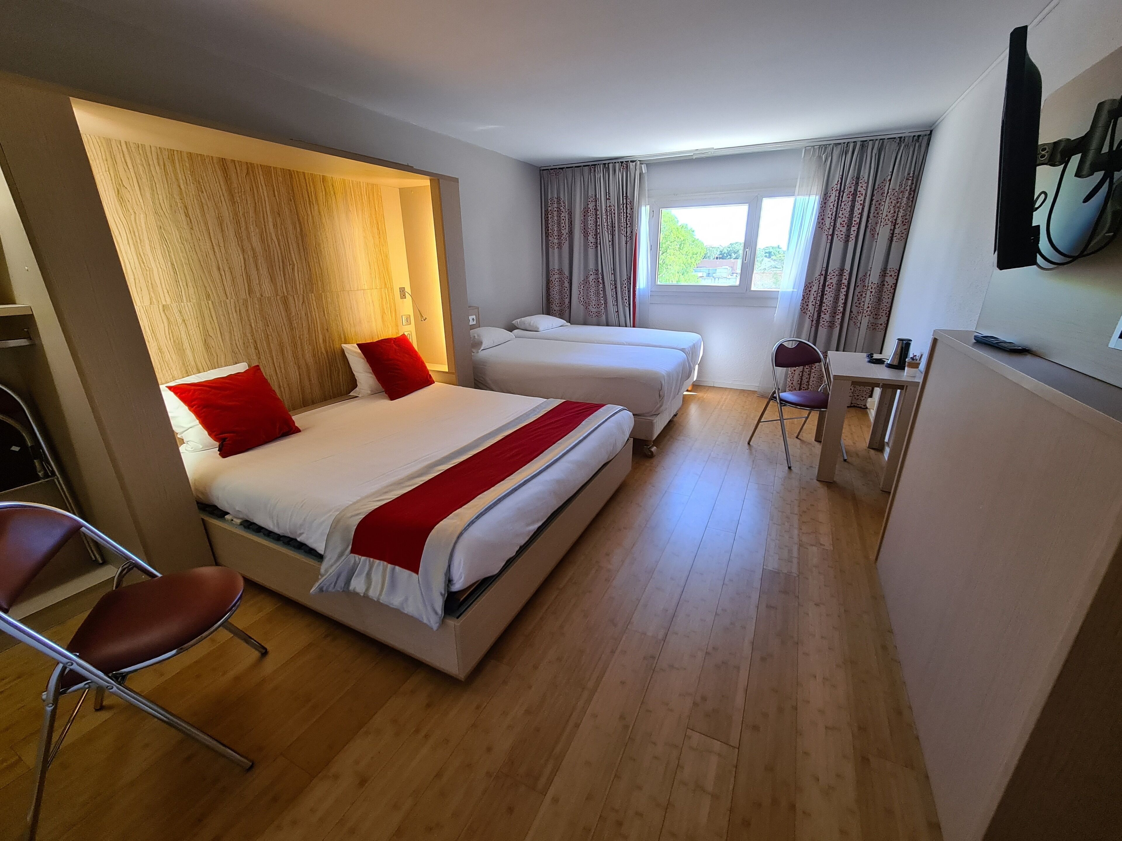 Une chambre d’hôtel avec deux lits, un bureau, une chaise et une fenêtre avec des rideaux.