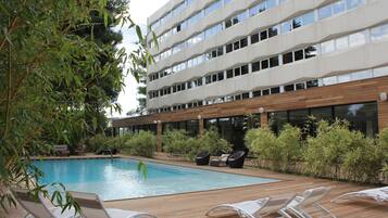 A modern hotel with a swimming pool, lounge chairs, and wooden deck.