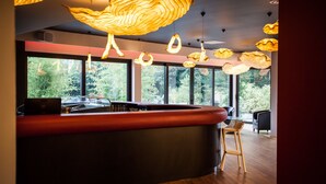 A modern bar area with a curved counter, large windows offering a view of greenery, and unique, textured pendant lighting. - C Suites (Nîmes)