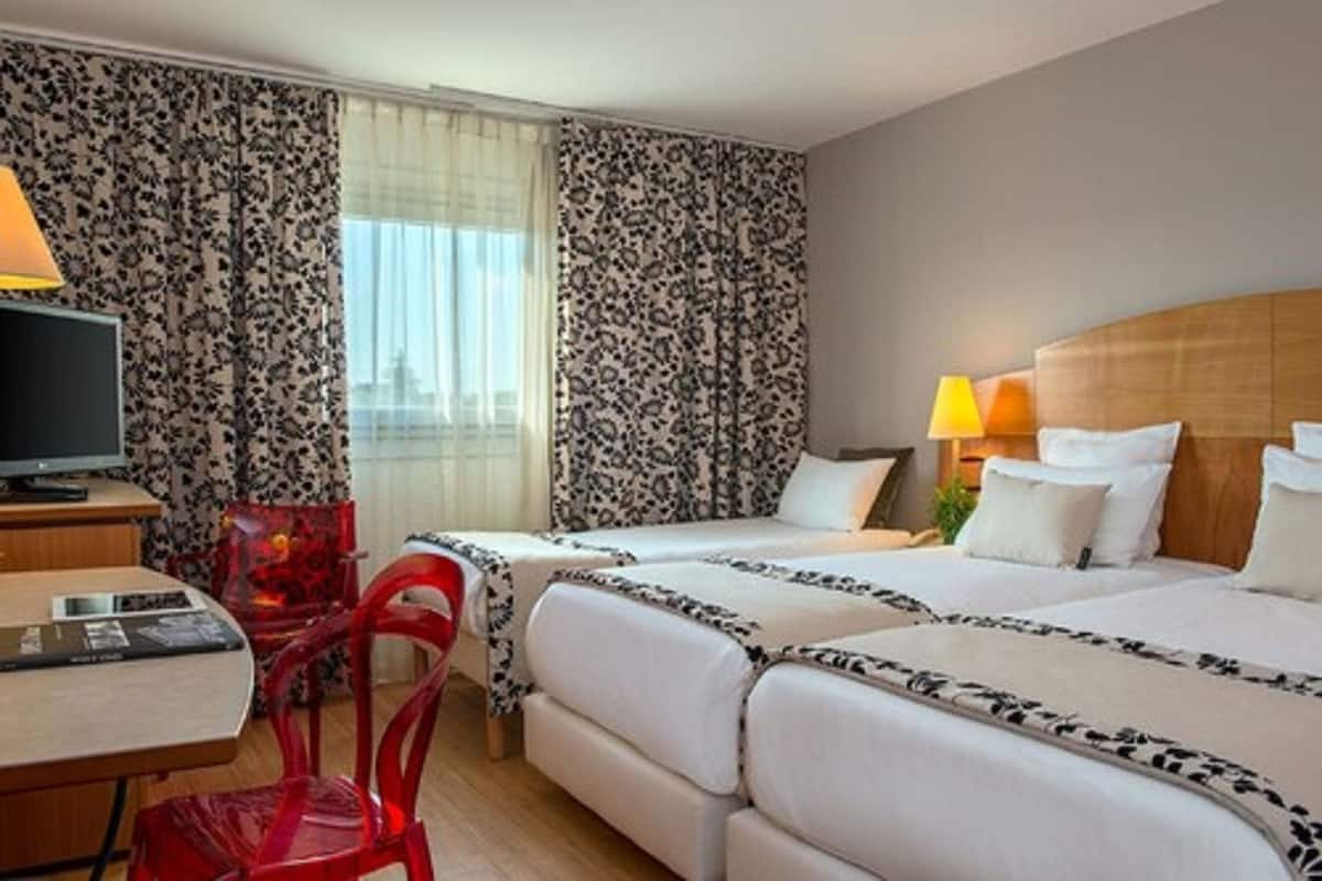 A hotel room with two beds, a desk, a TV, and a red chair.