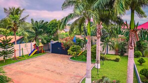 A paved courtyard with palm trees, a playground, and a building with a red roof.