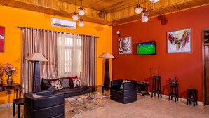 A living room with a wooden ceiling, a black sofa, a coffee table, and a TV on the wall.