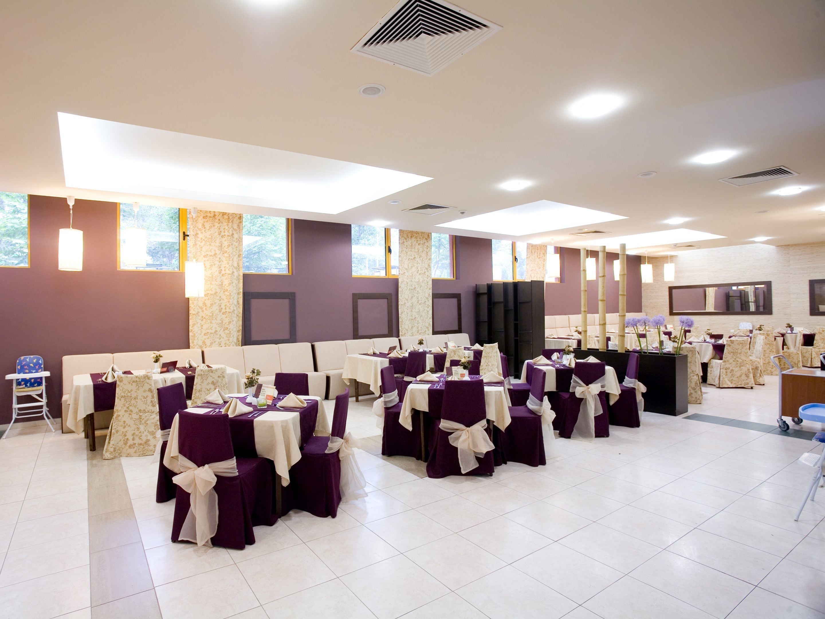 A banquet hall with multiple round tables, chairs, and a stage area.