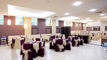 A banquet hall with multiple round tables, chairs, and a stage area.