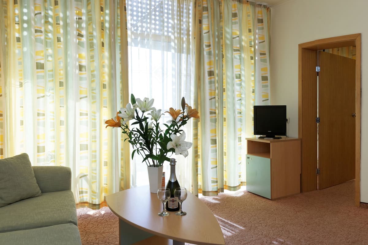 A living room with a sofa, a table with a vase of flowers, a television on a stand, and a door.