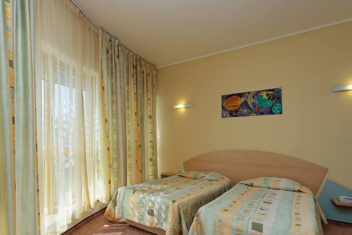 A hotel room with two beds, a painting on the wall, and a window with curtains.