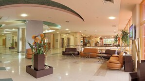 Eine geräumige Lobby mit einer zentralen Sitzecke, einem Empfangstresen und einer Bar/Lounge im Hintergrund.