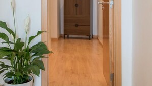 A hallway with a wooden floor, a potted plant, and a wooden cabinet with drawers. - Inn Fashion Residence (Lisbon)
