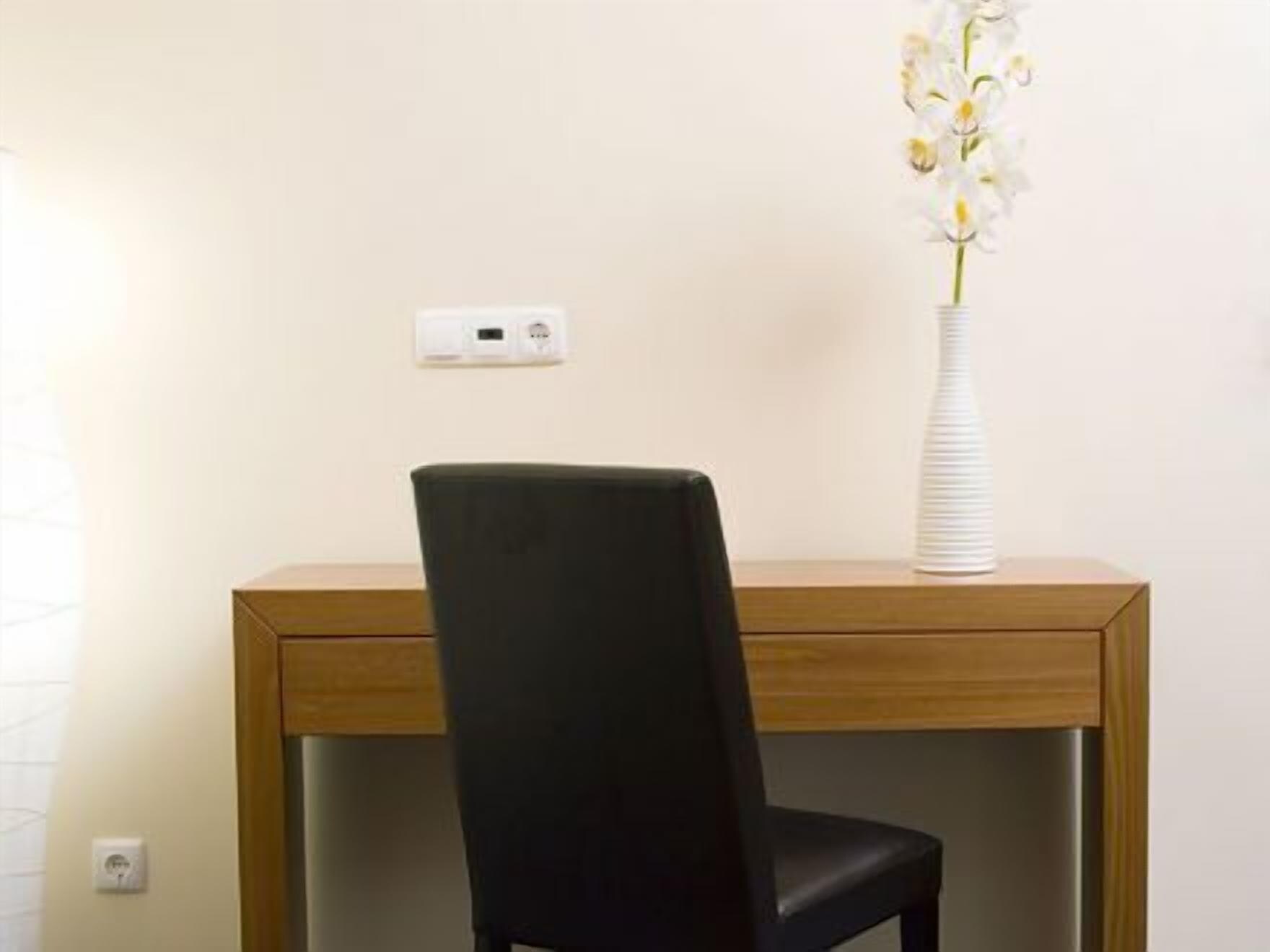 A room with a wooden desk, a black chair, and a white vase with flowers.