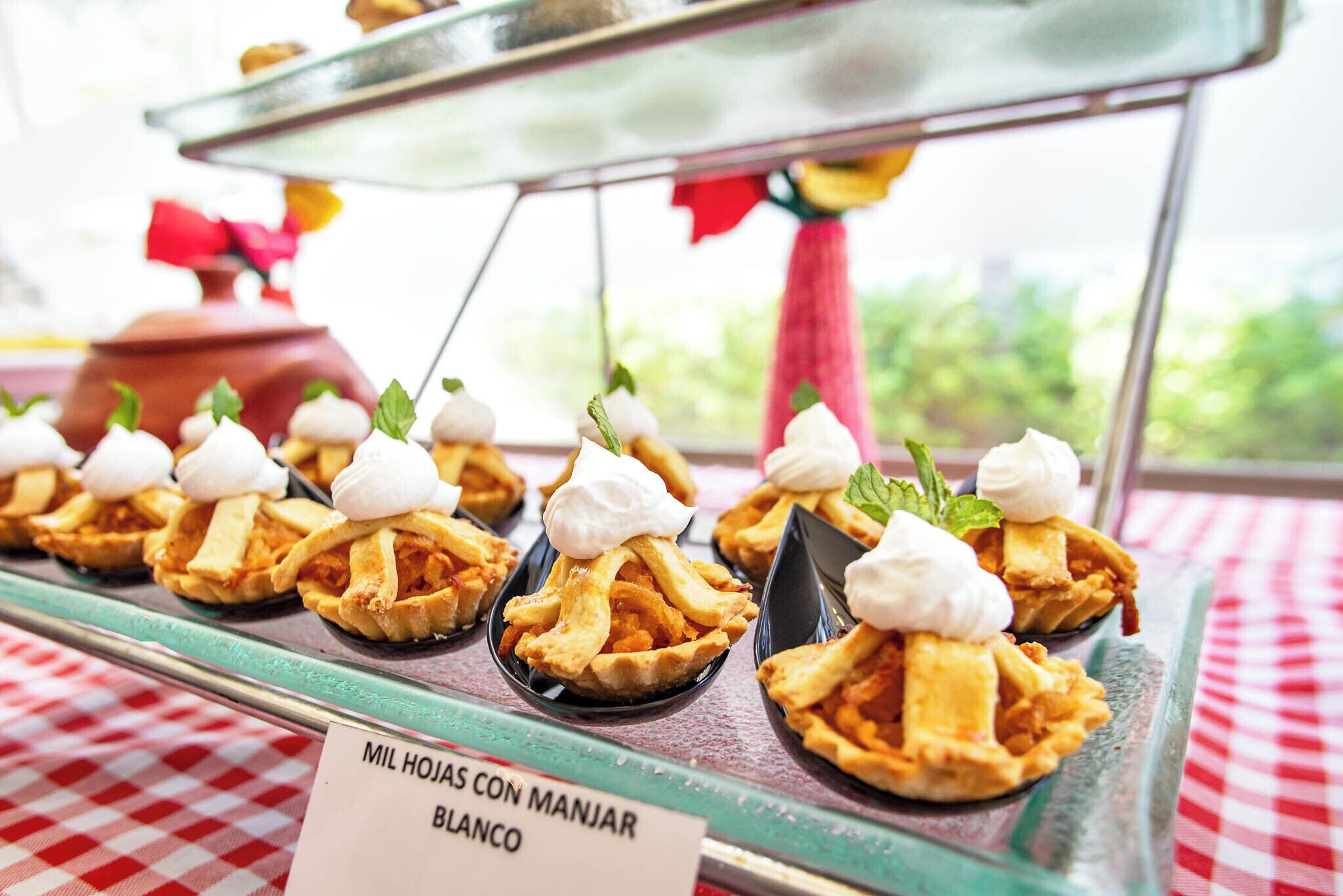 Una presentación de mini tartaletas con crema batida y hojas de menta, con el rótulo 'Mil Hojas Con Manjar Blanco'.