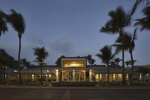 Un hotel moderno con un atrium central, palmeras y una entrada bien iluminada.