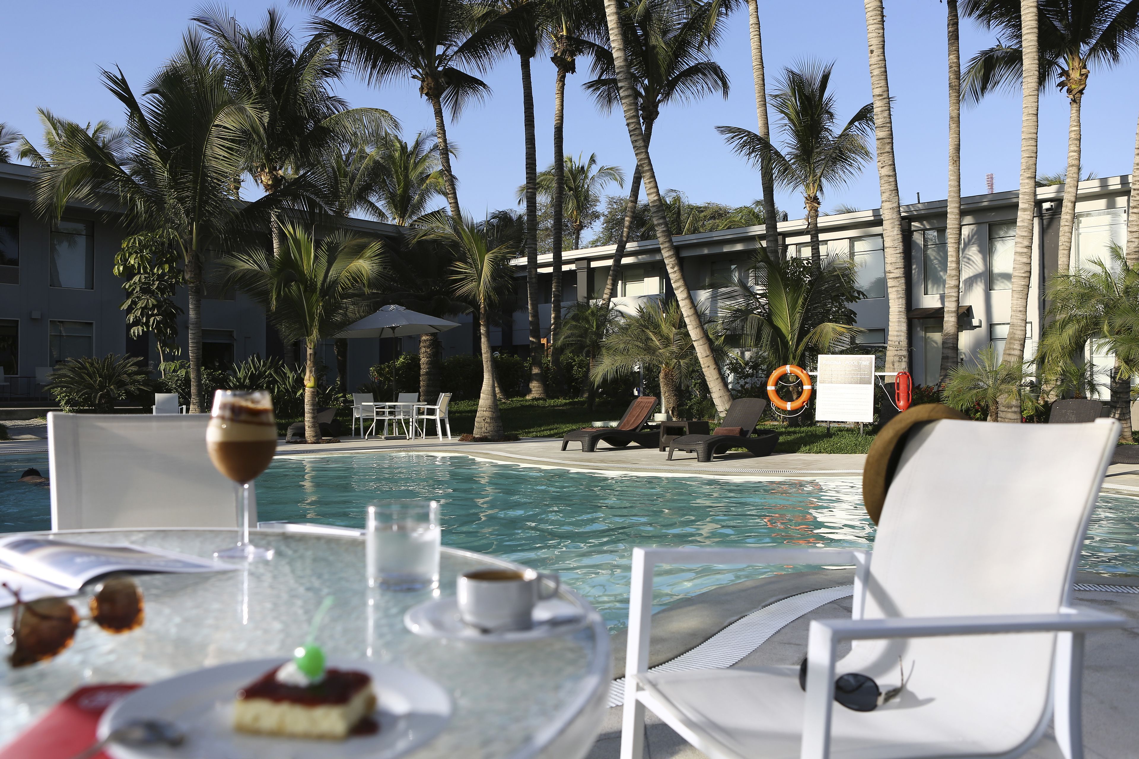 Blick auf ein Schwimmbecken mit einem für zwei Personen gedecktem Tisch, einer Nachspeise und einem Glas Wein.