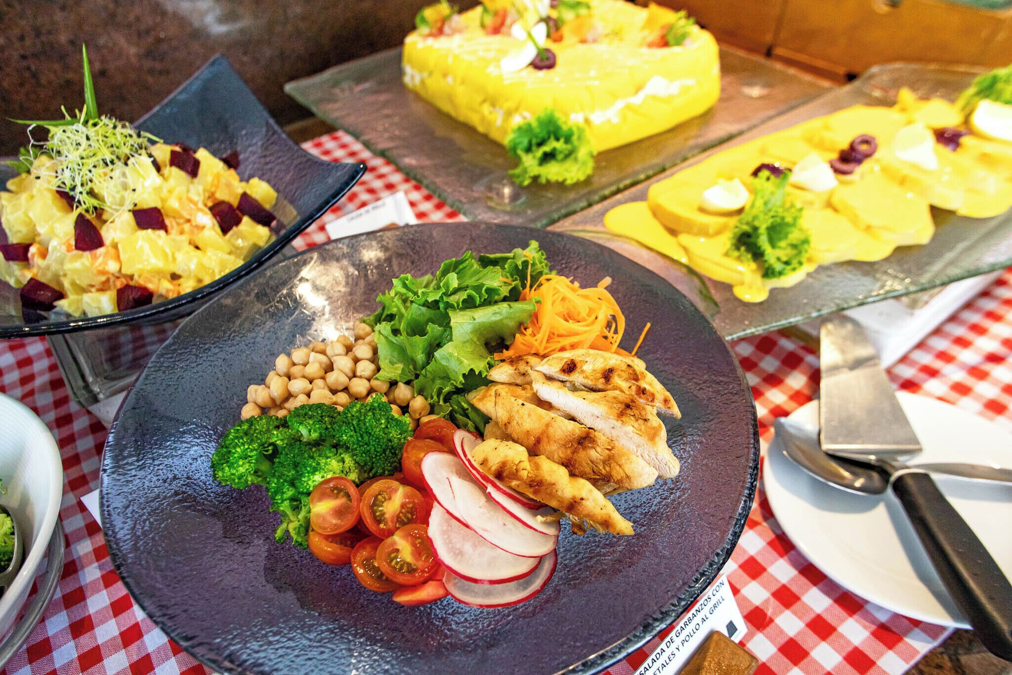 Un bufé con diversos platos, incluyendo ensaladas, pollo a la parrilla y un pastel.