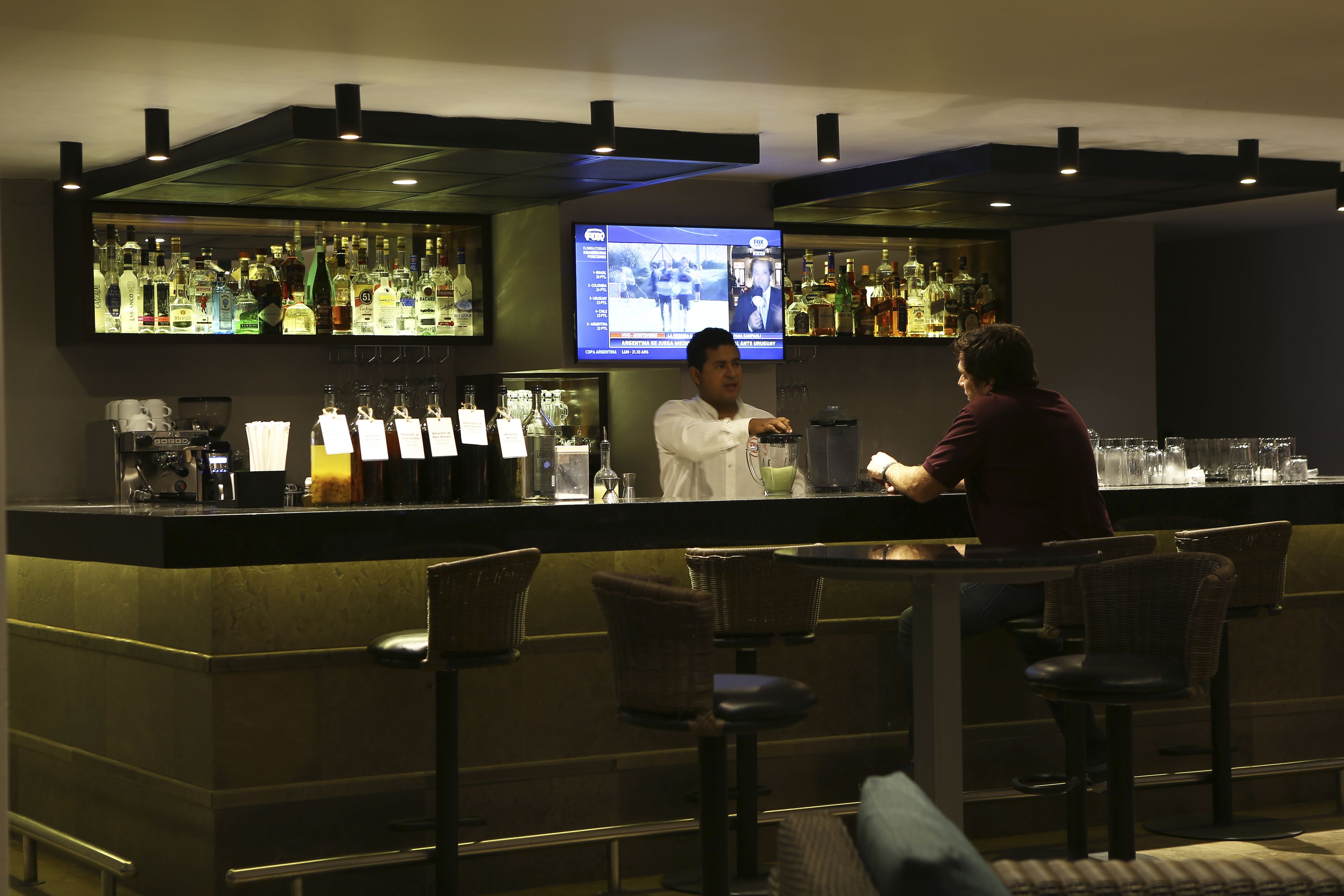Un espace bar comprenant un comptoir, des tabourets de bar et un écran de télévision diffusant un programme d’information.