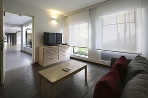 Una sala de estar moderna con un televisor de pantalla plana, una mesa de centro de madera y un sofá con cojines rojos.