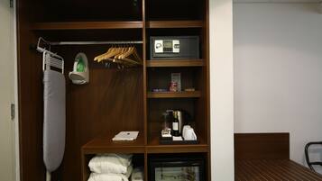 Habitación de hotel con armario que contiene una plancha, perchas, microondas, mini refrigerador con bebidas y una cama.