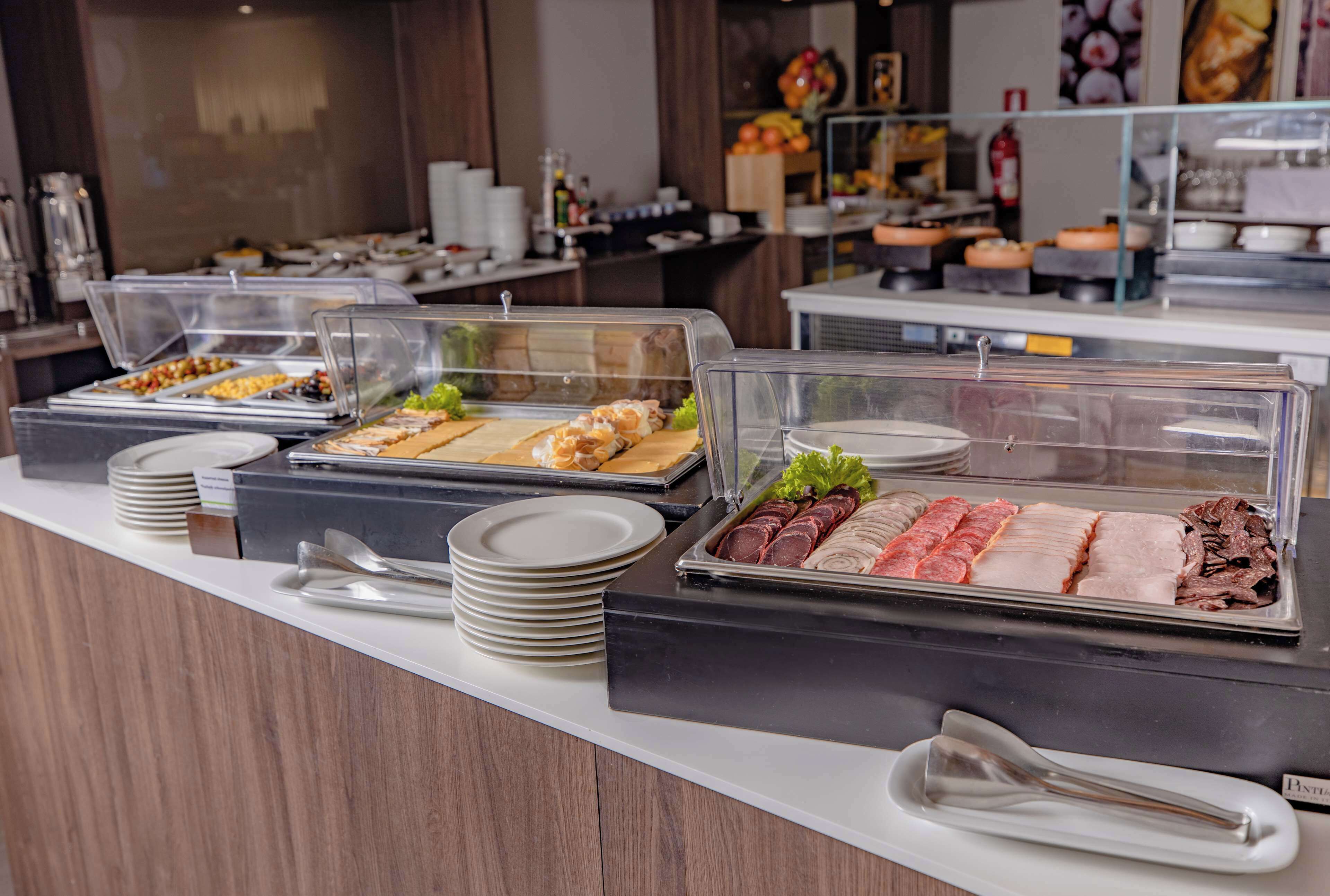 Un buffet proposant une variété de plats présentés dans des récipients transparents, notamment des viandes et des salades, avec des assiettes et des couverts à disposition sur le comptoir.