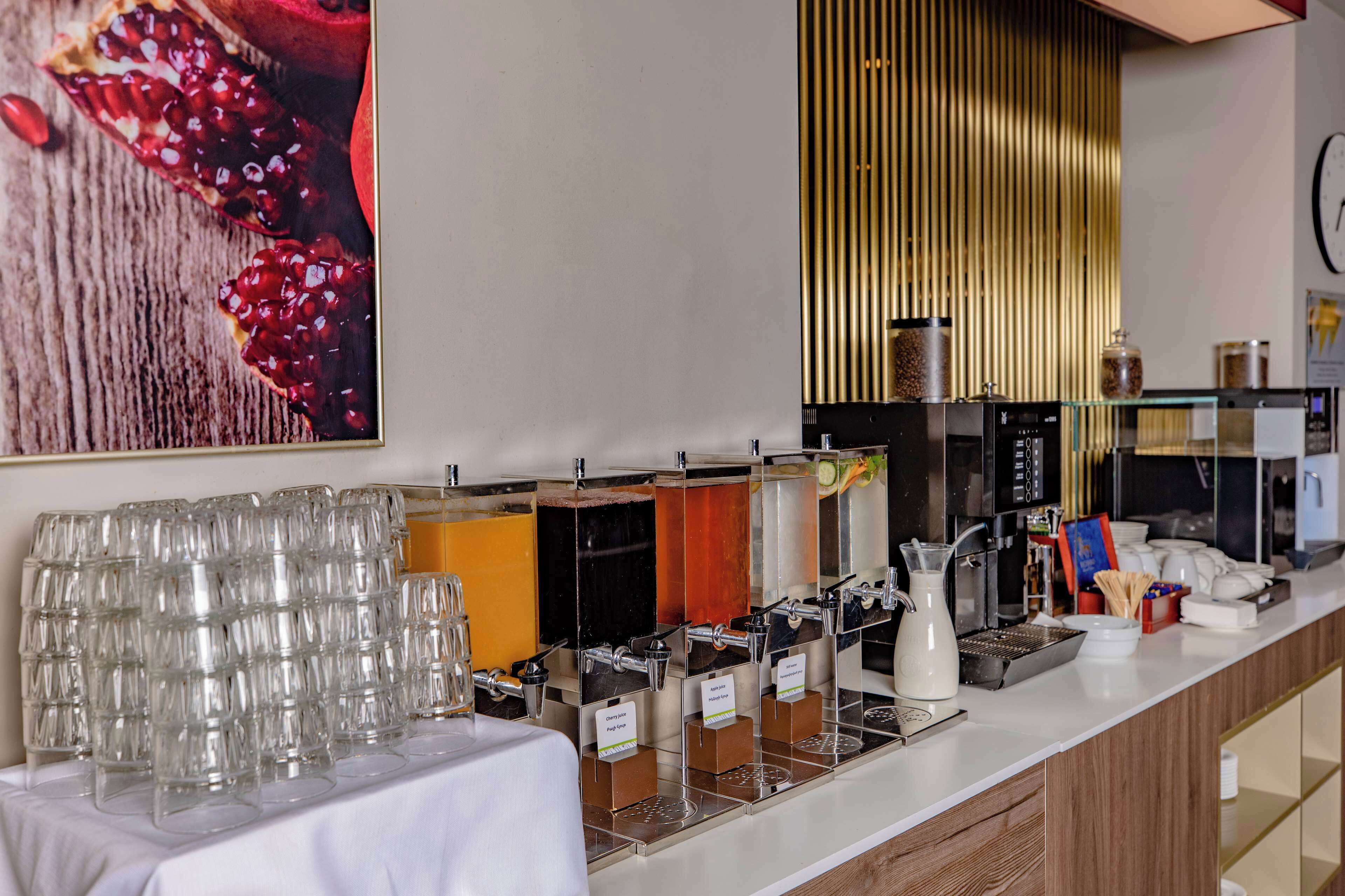 Ein Getränkeausgabebereich mit mehreren Spendern und einem Tisch mit gestapelten Gläsern.